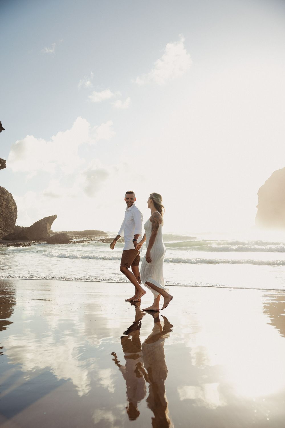 Couple walking on beach at sunset with reflections in wet sand. Auckland Wedding Photographer and videographer