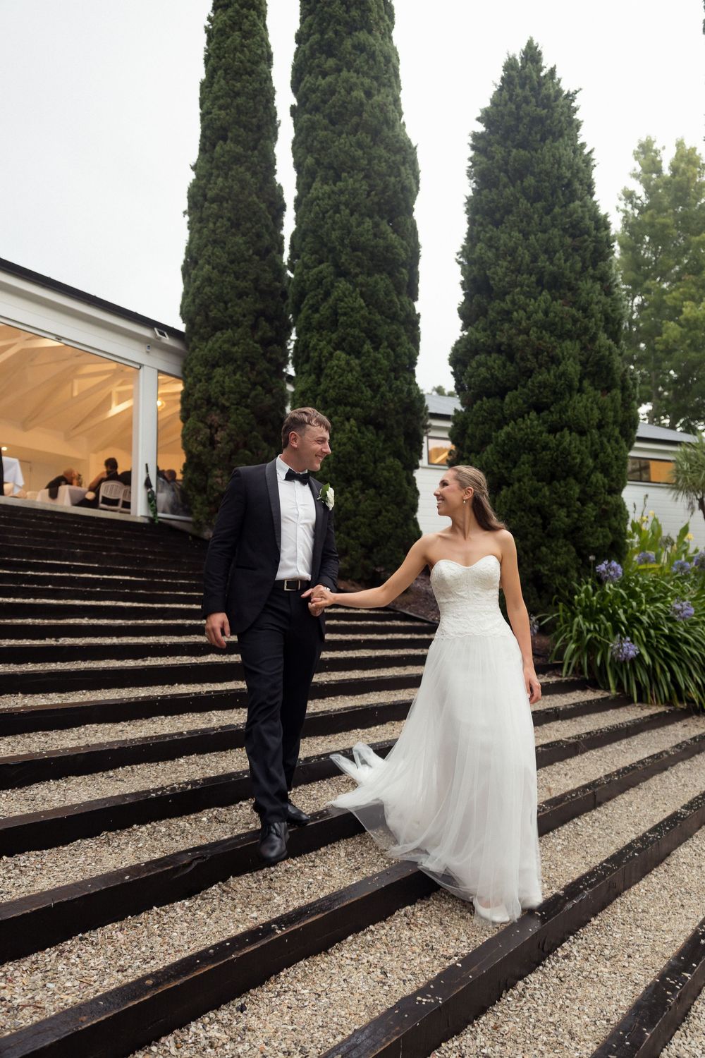 Couple descending grand outdoor staircase surrounded by tall cypress trees. Wedding Photographer and videographer. Bridgewater estate