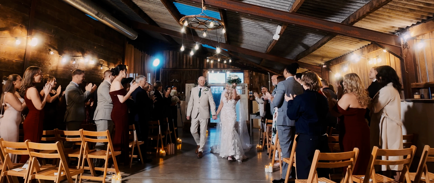 Guests dance and celebrate at a rustic barn wedding reception with twinkling lights overhead.