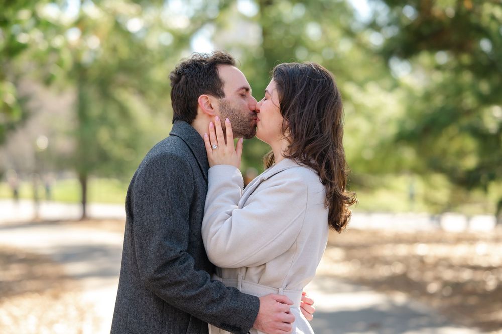 A romantic couple sharing a tender kiss outdoors in a park on a sunny autumn day.