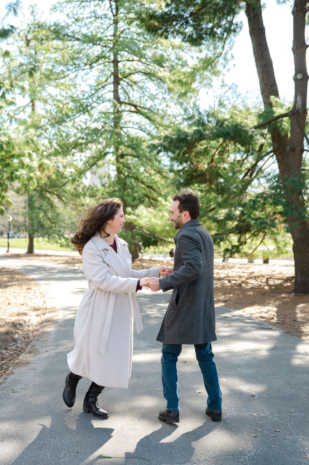 A couple in casual attire playfully interacting on a tree-lined path on a sunny autumn day.