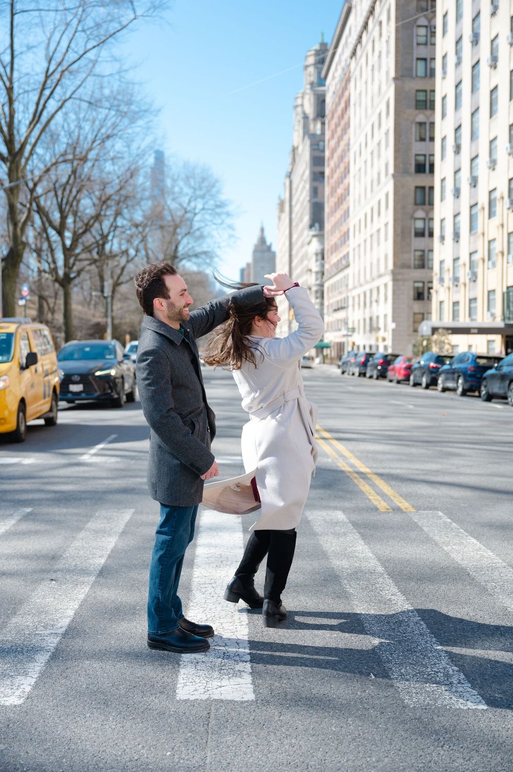 A couple recreates a playful dance pose on a crosswalk in an urban street with tall apartment buildings in the background.