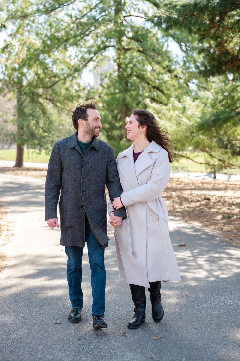 A couple walks together on a tree-lined path while sharing a loving moment in casual winter attire.