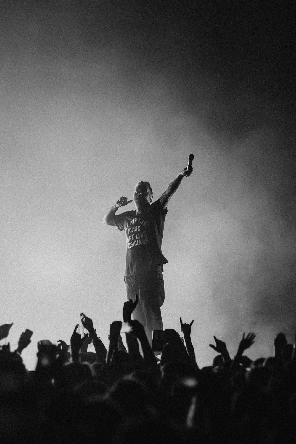 Silhouettes of performers and crowd at a concert with dramatic backlighting creating a moody black and white atmosphere.