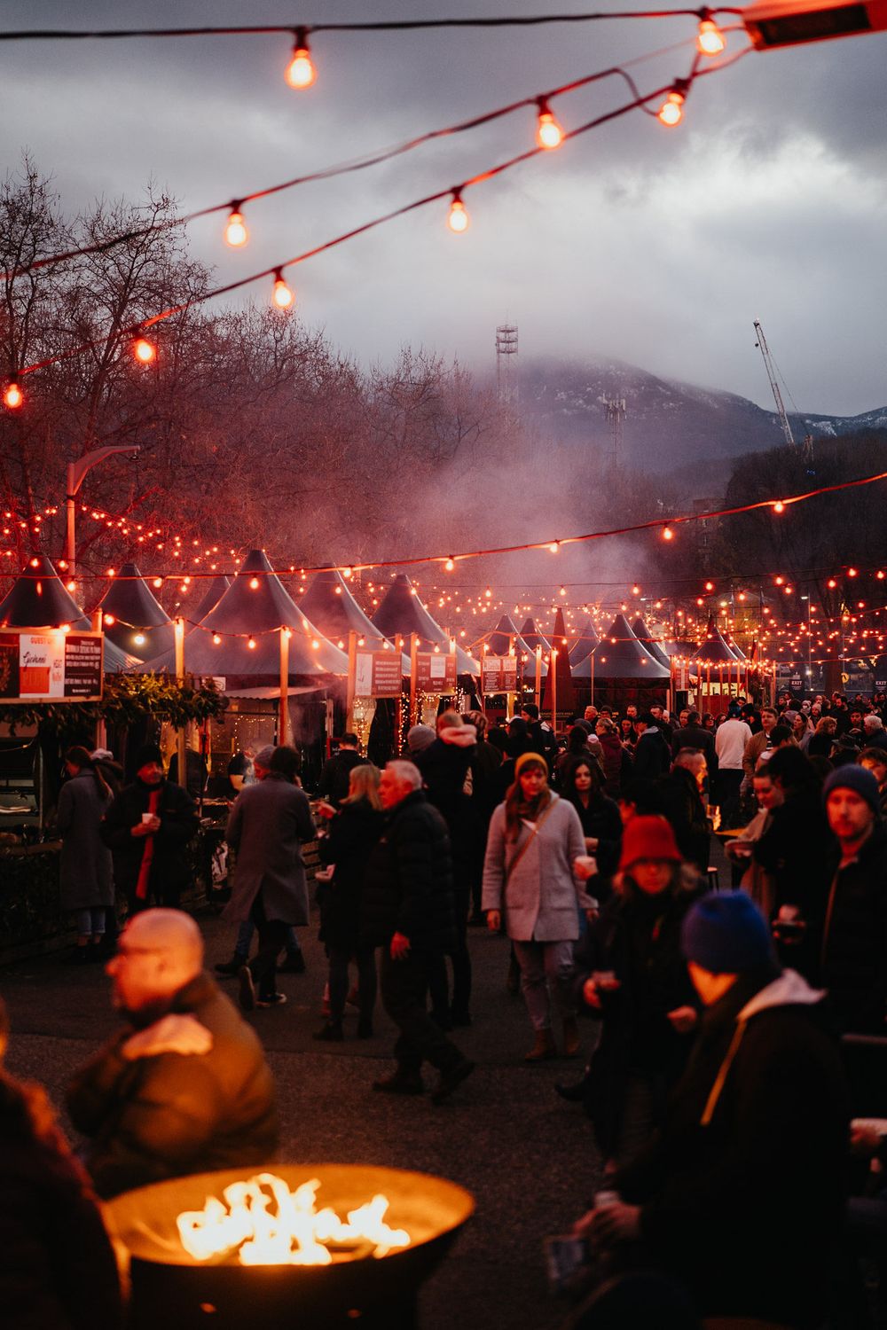 Outdoor evening gathering with red string lights illuminating a crowd beneath moody storm clouds.