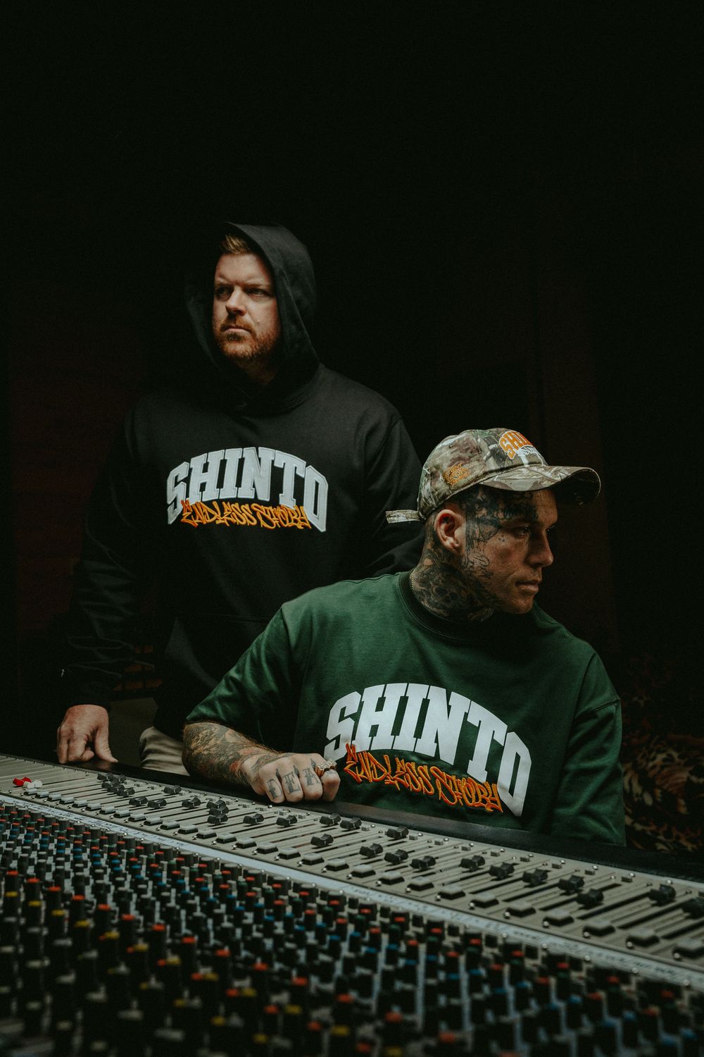 Music producer working at a professional mixing console in dark studio environment wearing a black hoodie.