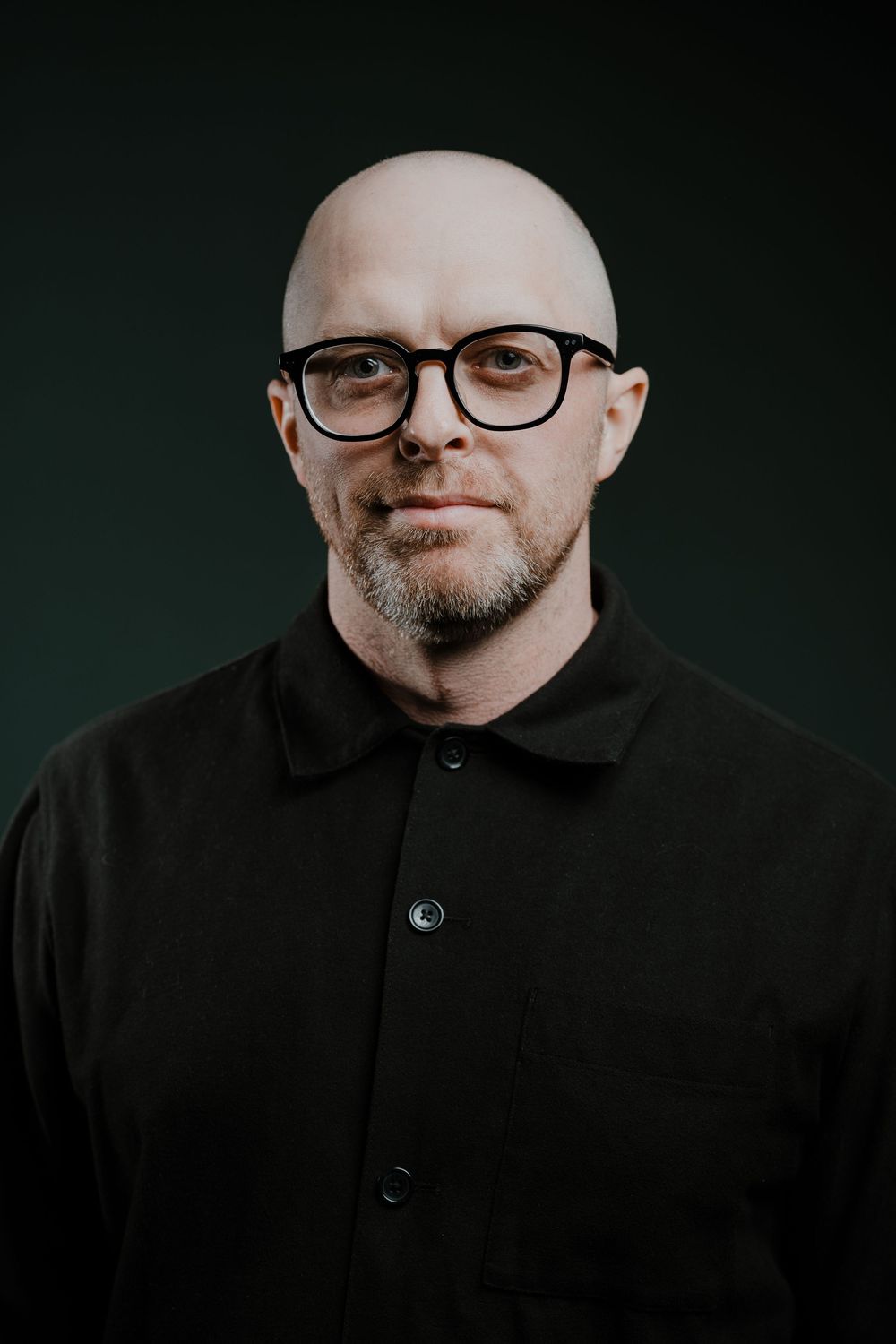 A series of dark, moody portraits showing a person wearing glasses and black clothing against a dark background.