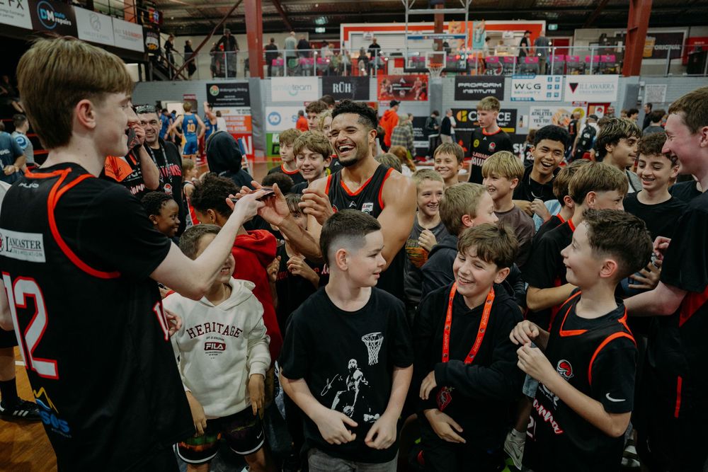 Basketball player celebrates with excited youth players at indoor sports event, high-fiving and cheering together.