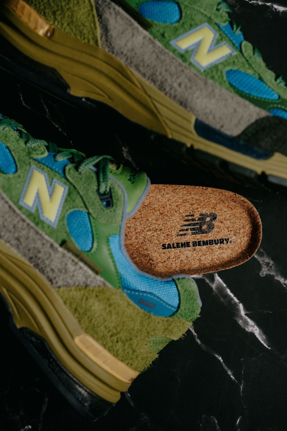 New Balance sneakers in green and blue with cork insole detail on black marble surface.