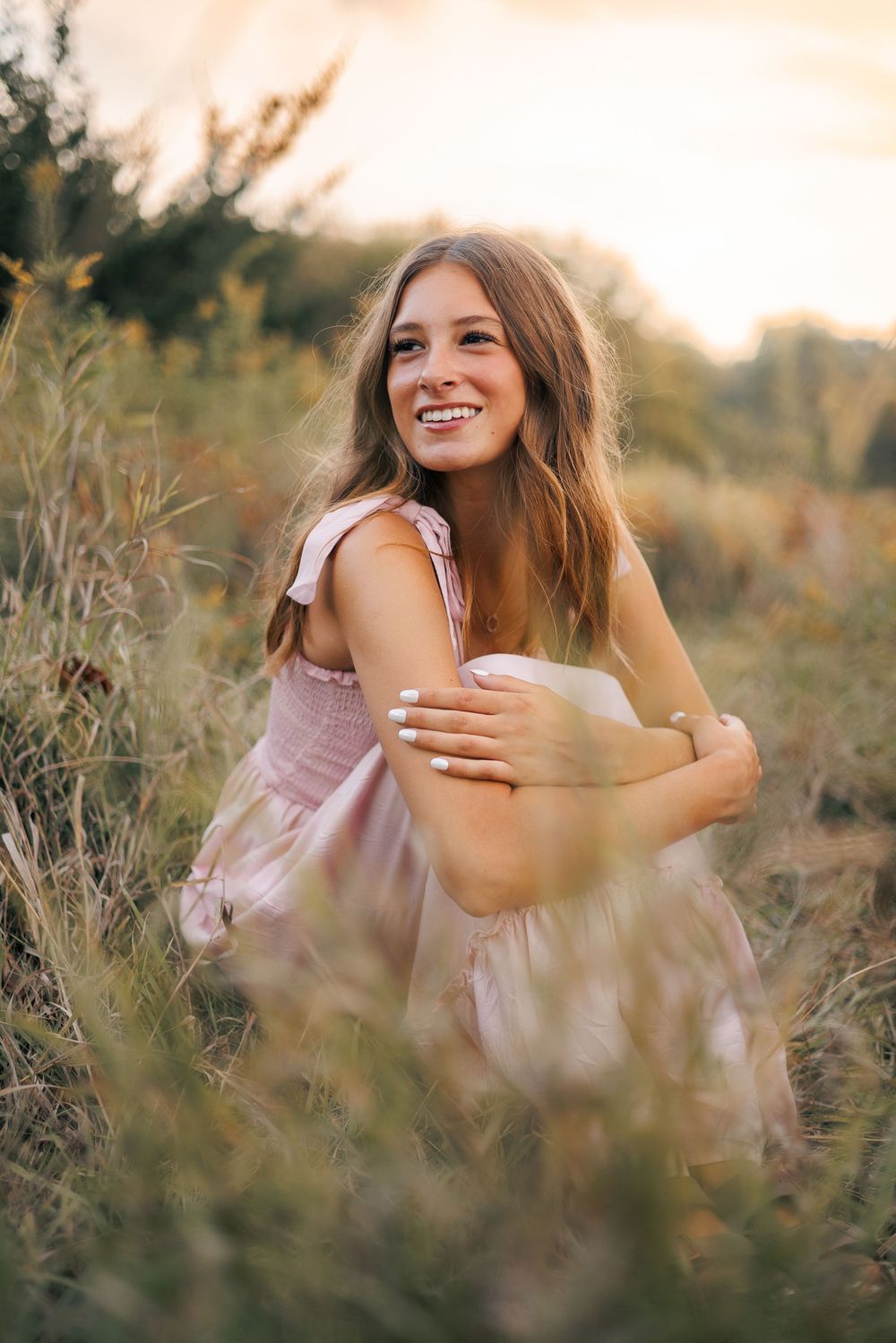 Dreamy outdoor portrait series in a meadow at sunset with soft pink dress and tall grasses creating ethereal atmosphere.