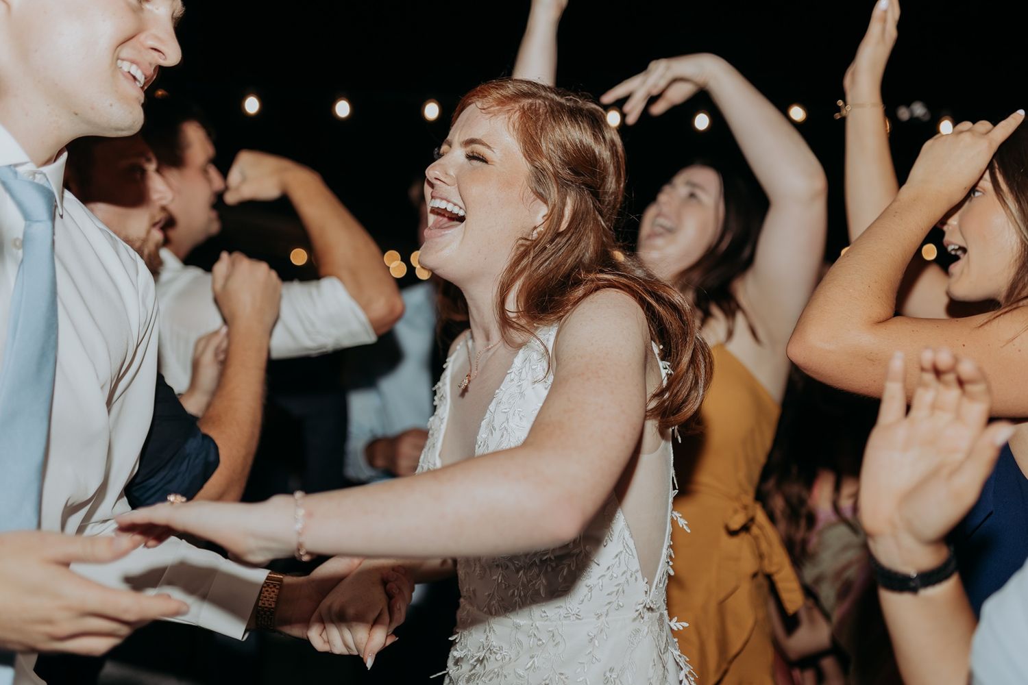 Joyful wedding guests dancing and laughing together at a lively outdoor reception party at night at Rancho Buena Vista Adobe.