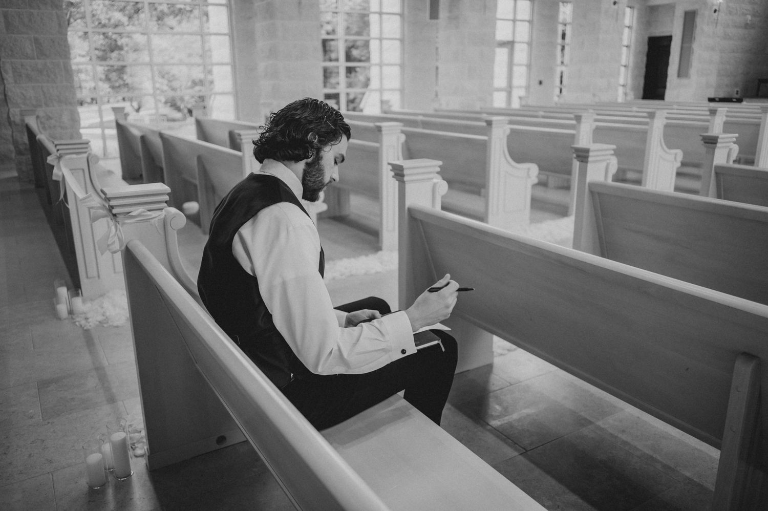 A person sits alone in a church pew reading in black and white vintage photograph.