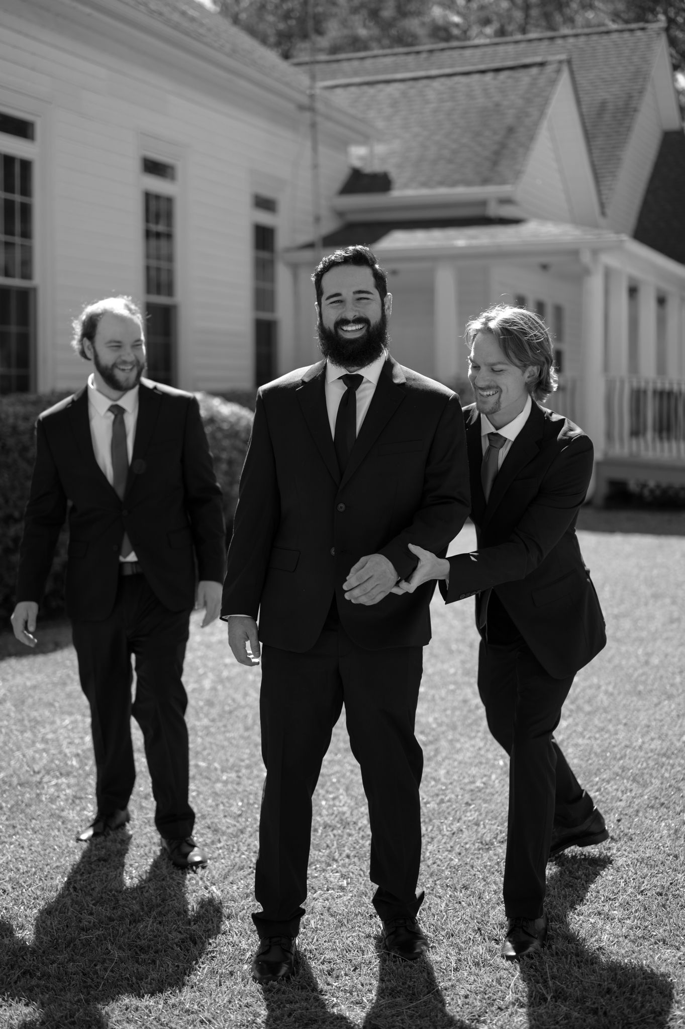 Black and white photo sequence of groomsmen in suits walking and laughing together outdoors.