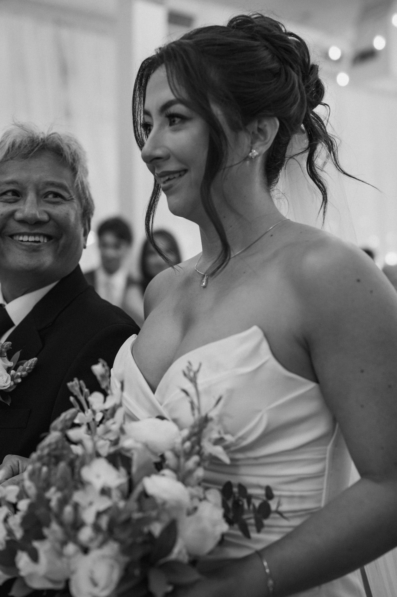 A bride in a white strapless gown holds a bouquet and shares joyful moments at a wedding reception.
