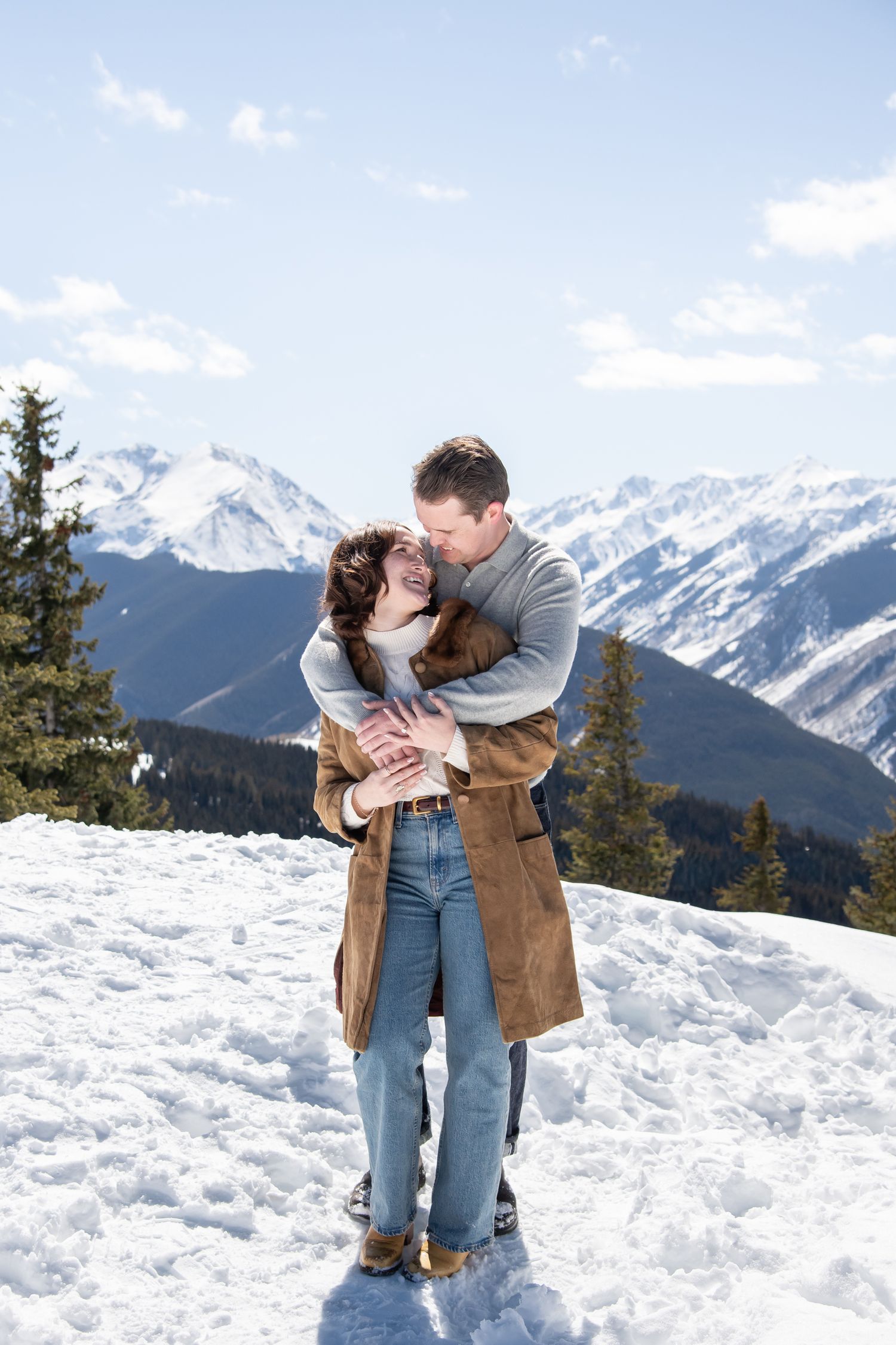 A couple shares a romantic moment against a stunning backdrop of snow-covered mountains in Aspen Colorado for winter engagement.