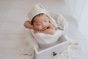 A newborn baby sleeps peacefully in a white swaddle blanket during a professional photography session.在專業攝影過程中，一名新生兒裹在白色襁褓毯里安然入睡。