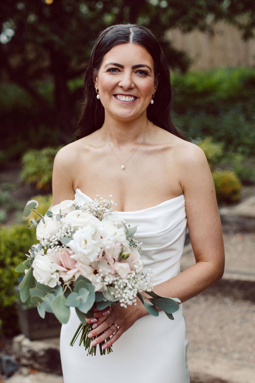 Beautiful wedding bouquet featuring white and blush pink flowers with eucalyptus held against an elegant white dress.