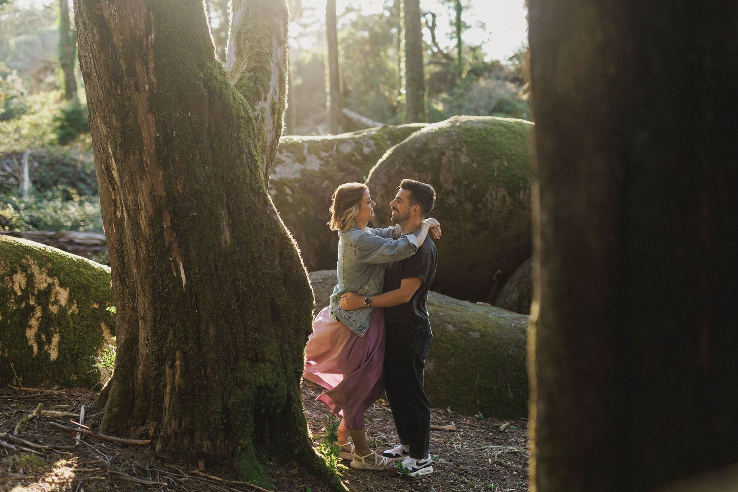Romantic couple embracing among mossy rocks during engagement session in Sintra forest near Peninha, Portugal