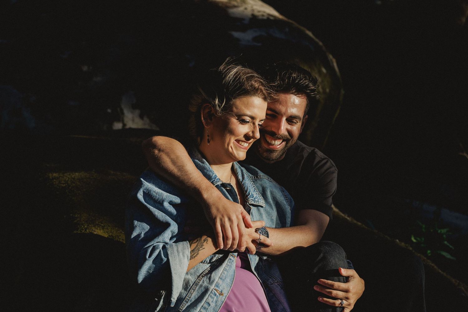 Intimate couple sitting together on rocks in golden light during engagement session in Sintra forest, Portugal