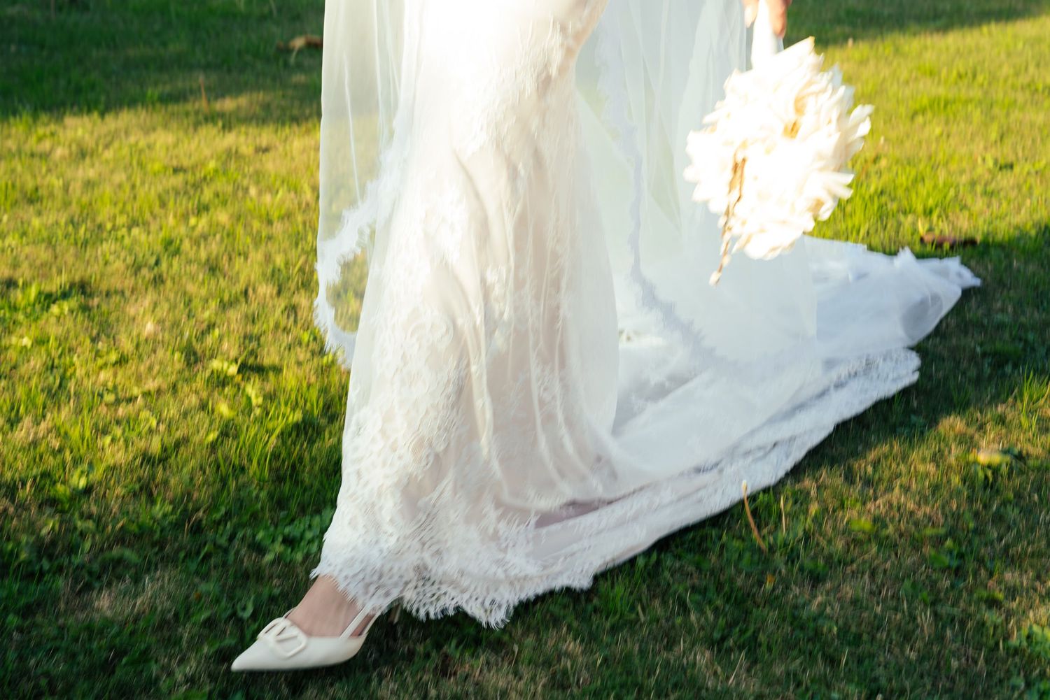 A flowing white wedding dress twirls gracefully on a sunny green lawn during a photo session.