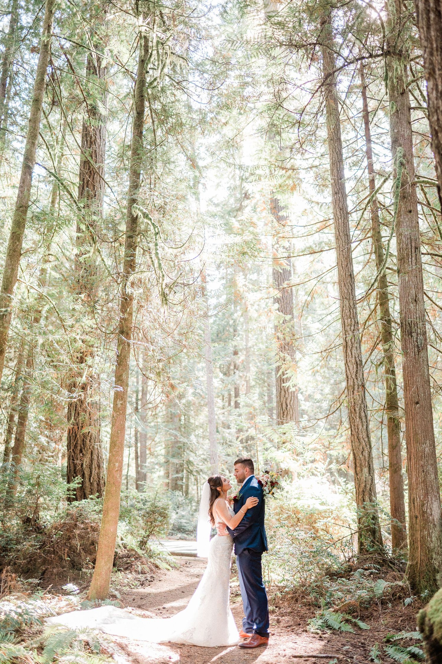 A couple shares a romantic moment on a rocky beach with evergreen forest-covered mountains in the background. Photo by Pine + Vow