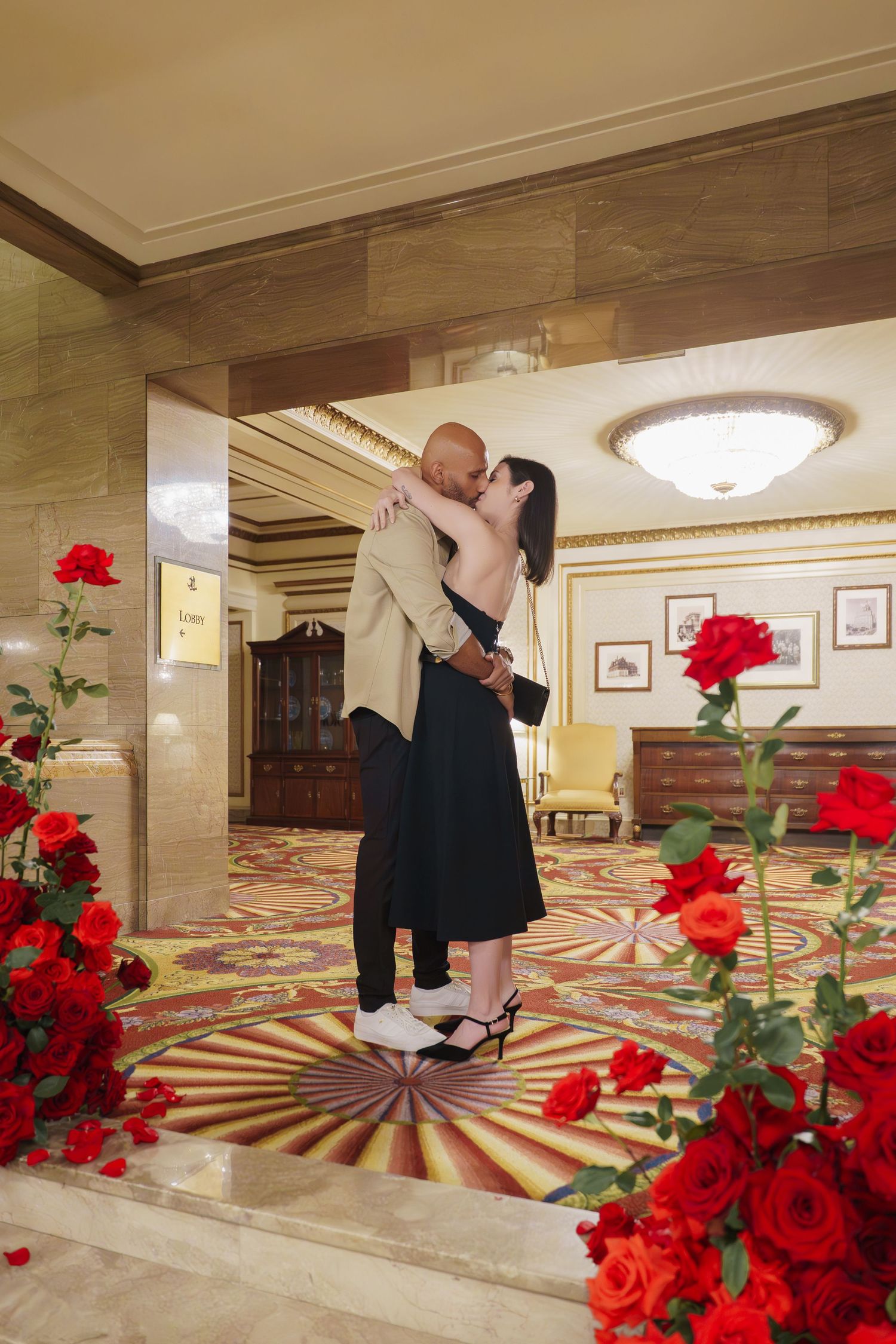 Red roses decorate a hotel hallway with a geometric patterned carpet and warm lighting.