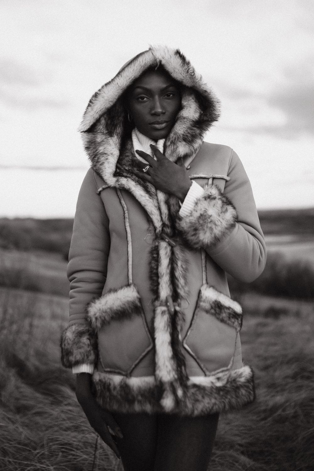 Black and white portrait series showing person in fur-trimmed winter coat against moody outdoor landscape.