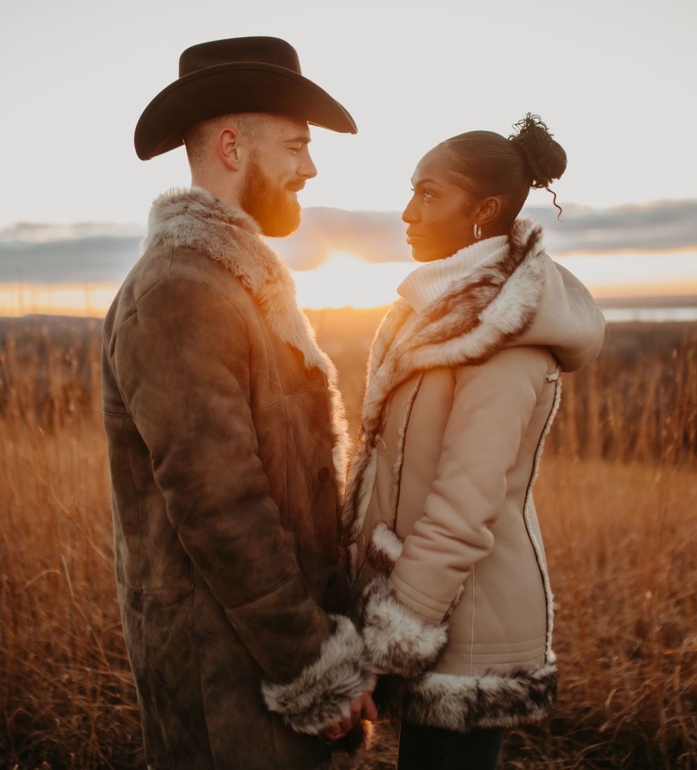 Romantic couple in winter coats embrace in golden field during sunset.