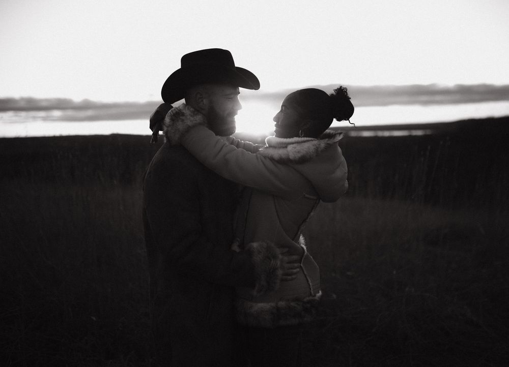 A silhouetted couple embracing in a tender moment against a dusky landscape.