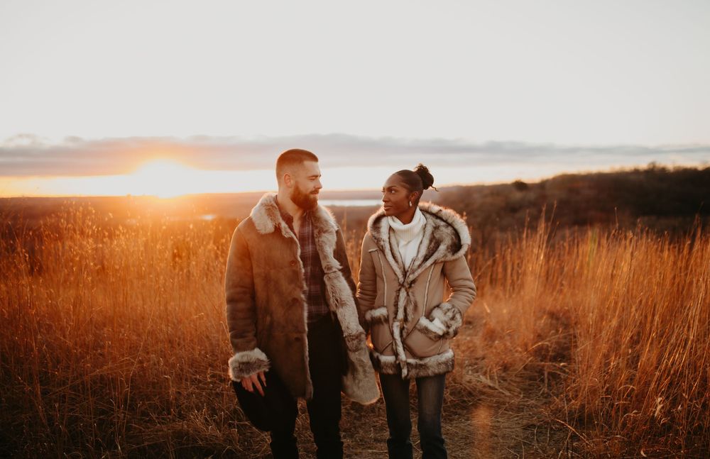 A romantic couple walks through a golden field at sunset creating a warm silhouette against the glowing sky.