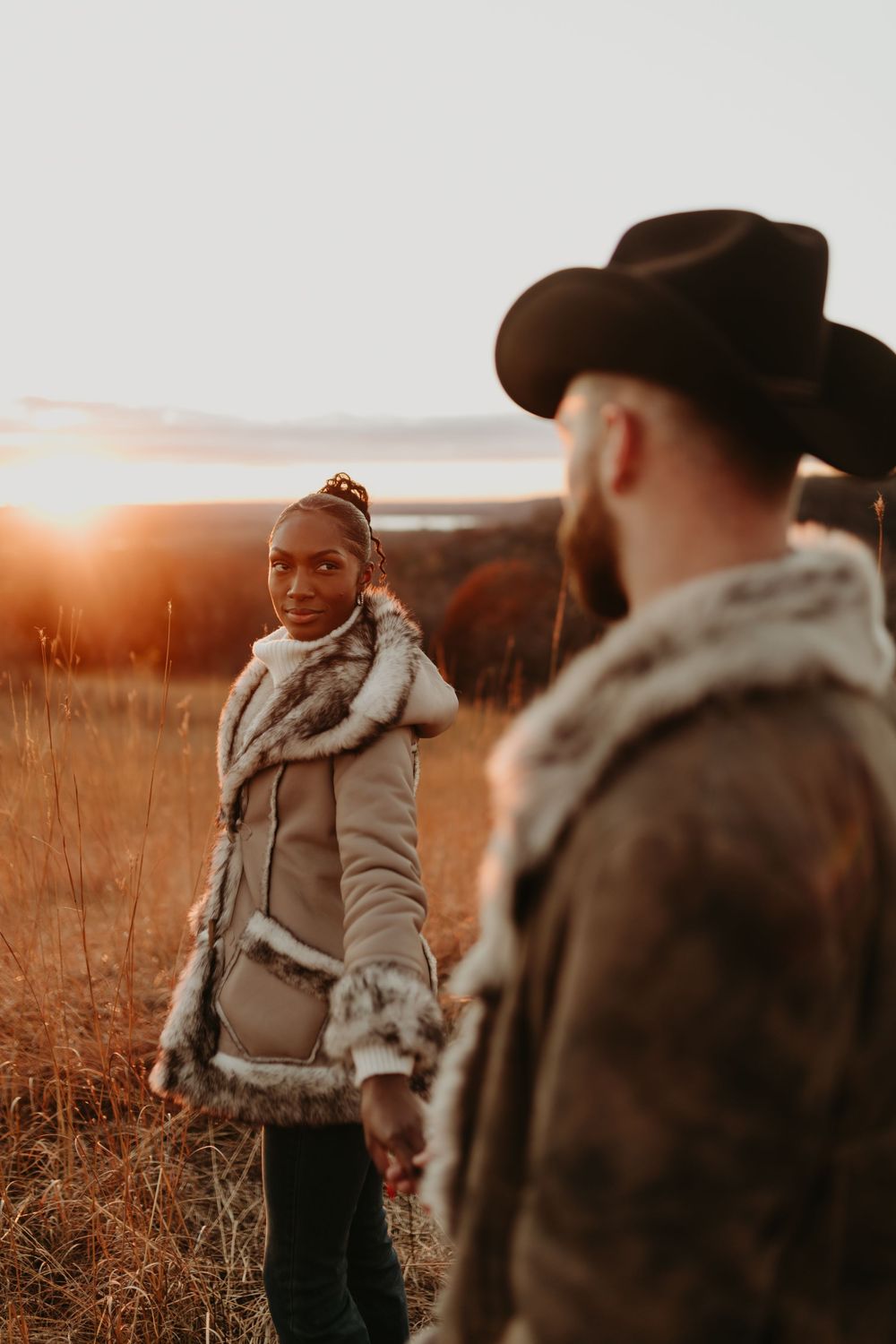 Two people in warm winter coats having a conversation in a field during golden hour.