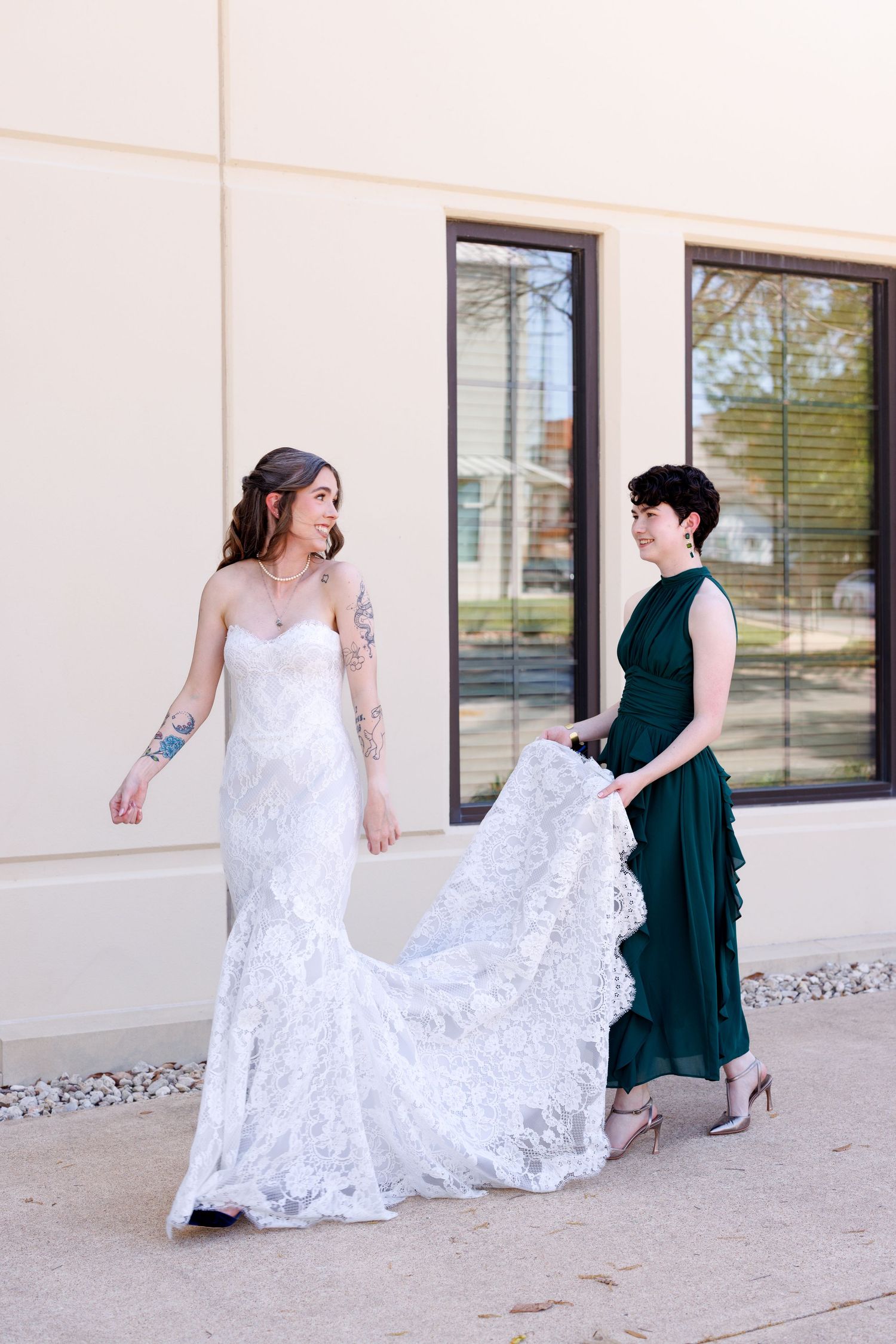 Two women in contrasting white and dark green dresses pose together in a series of playful photos against a light wall.