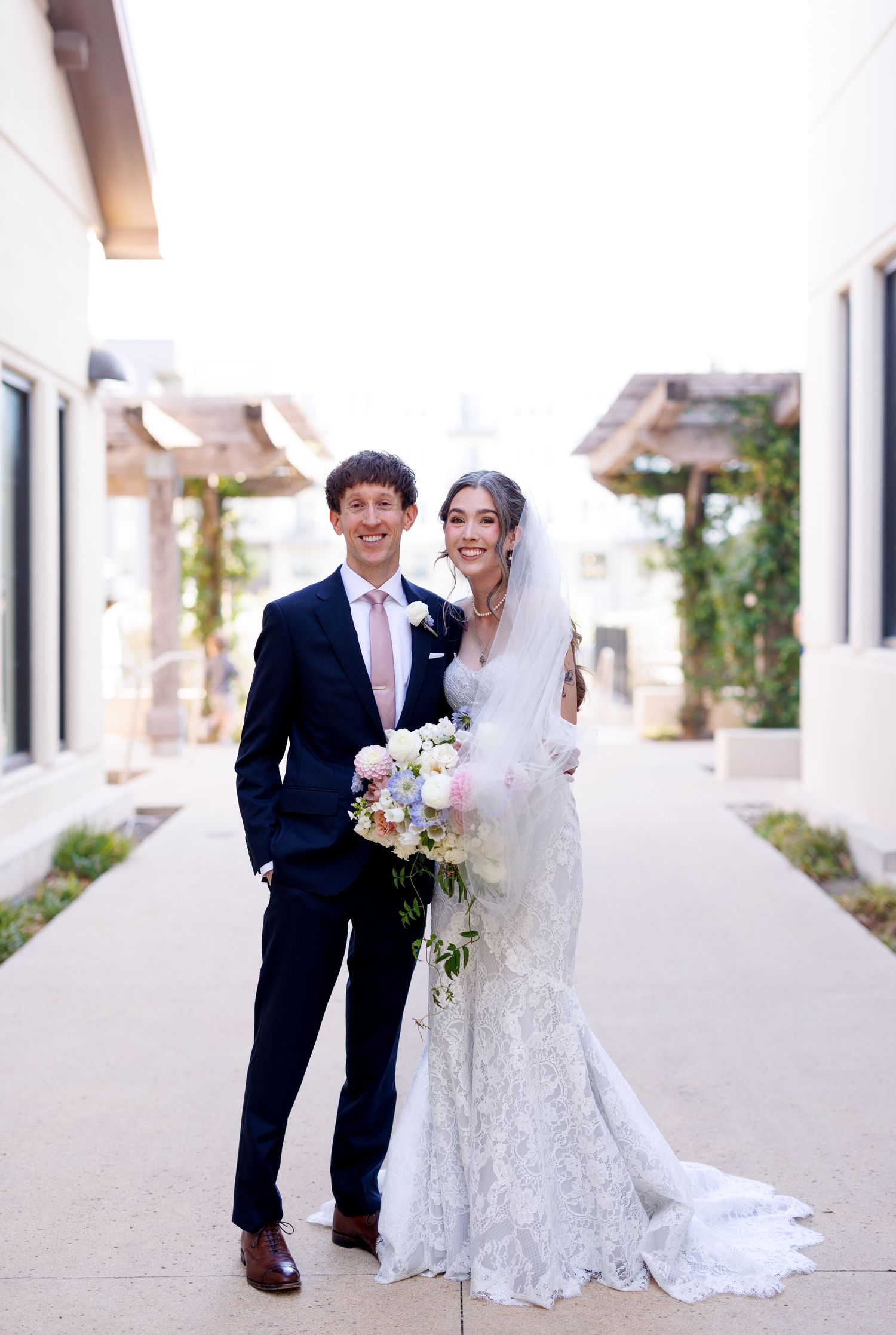A bride and groom share joyful moments together in a bright white hallway wearing formal wedding attire.