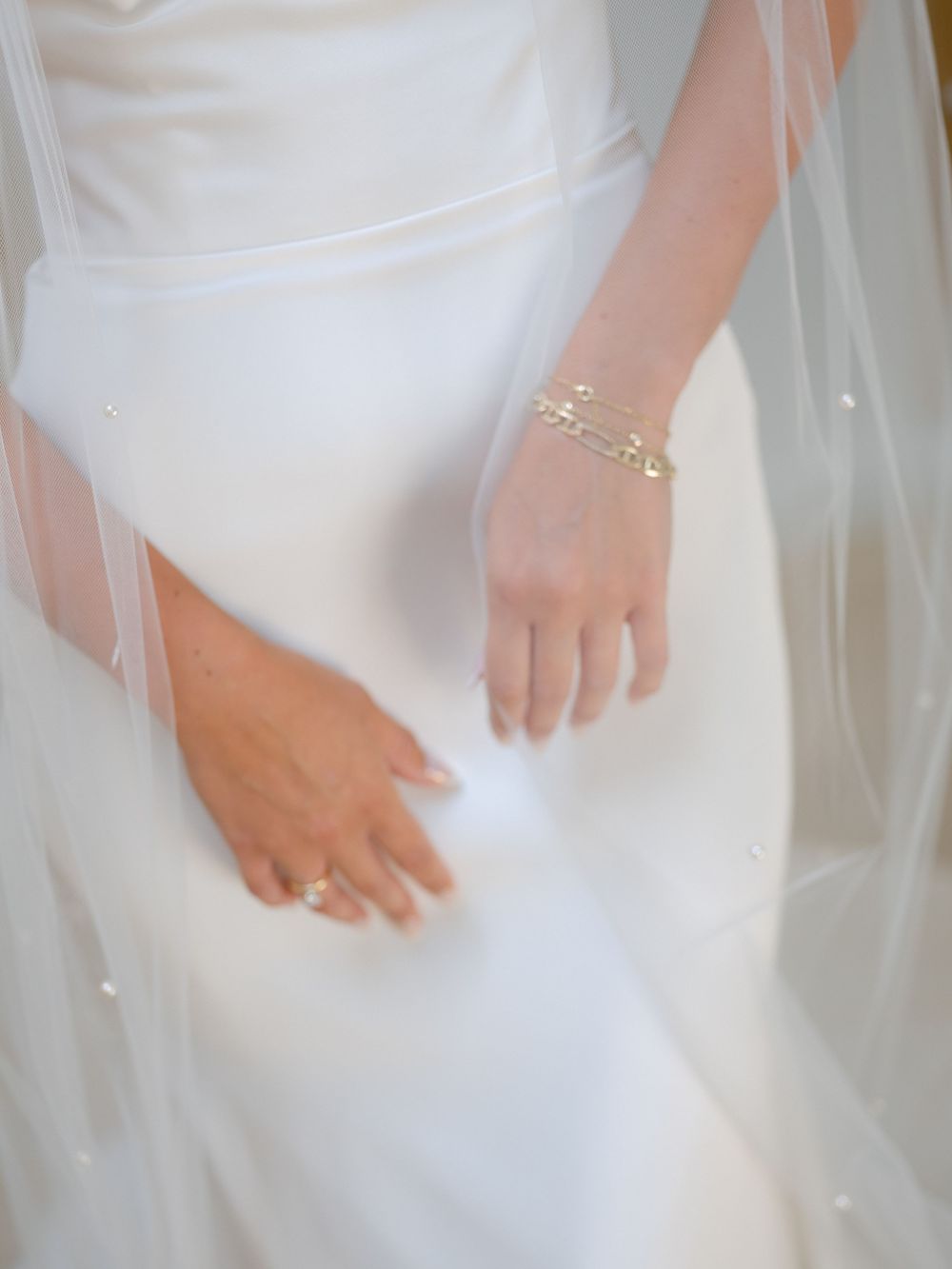 Elegant white bridal dress details with flowing tulle fabric and hands gracefully positioned against the gown.