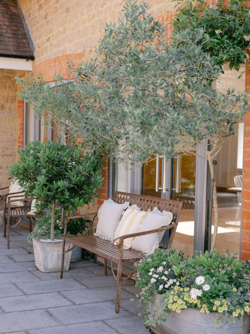 A tranquil patio area with wooden benches and potted olive trees creates a Mediterranean-inspired outdoor seating space.