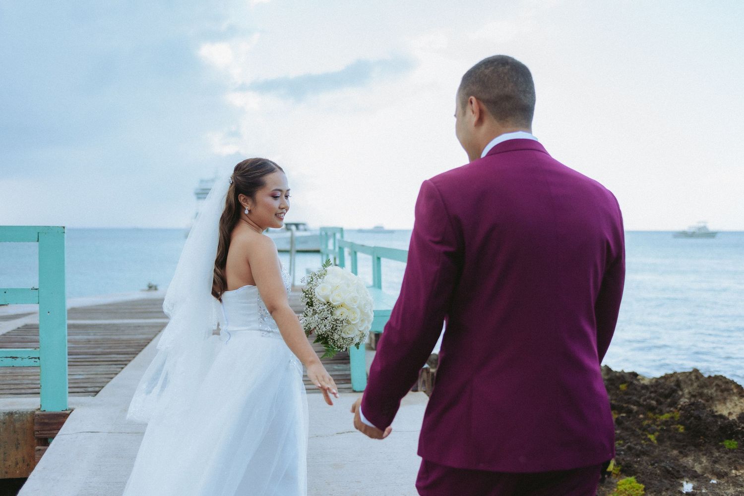 A couple in wedding attire walks along a scenic oceanfront path during their destination wedding ceremony.