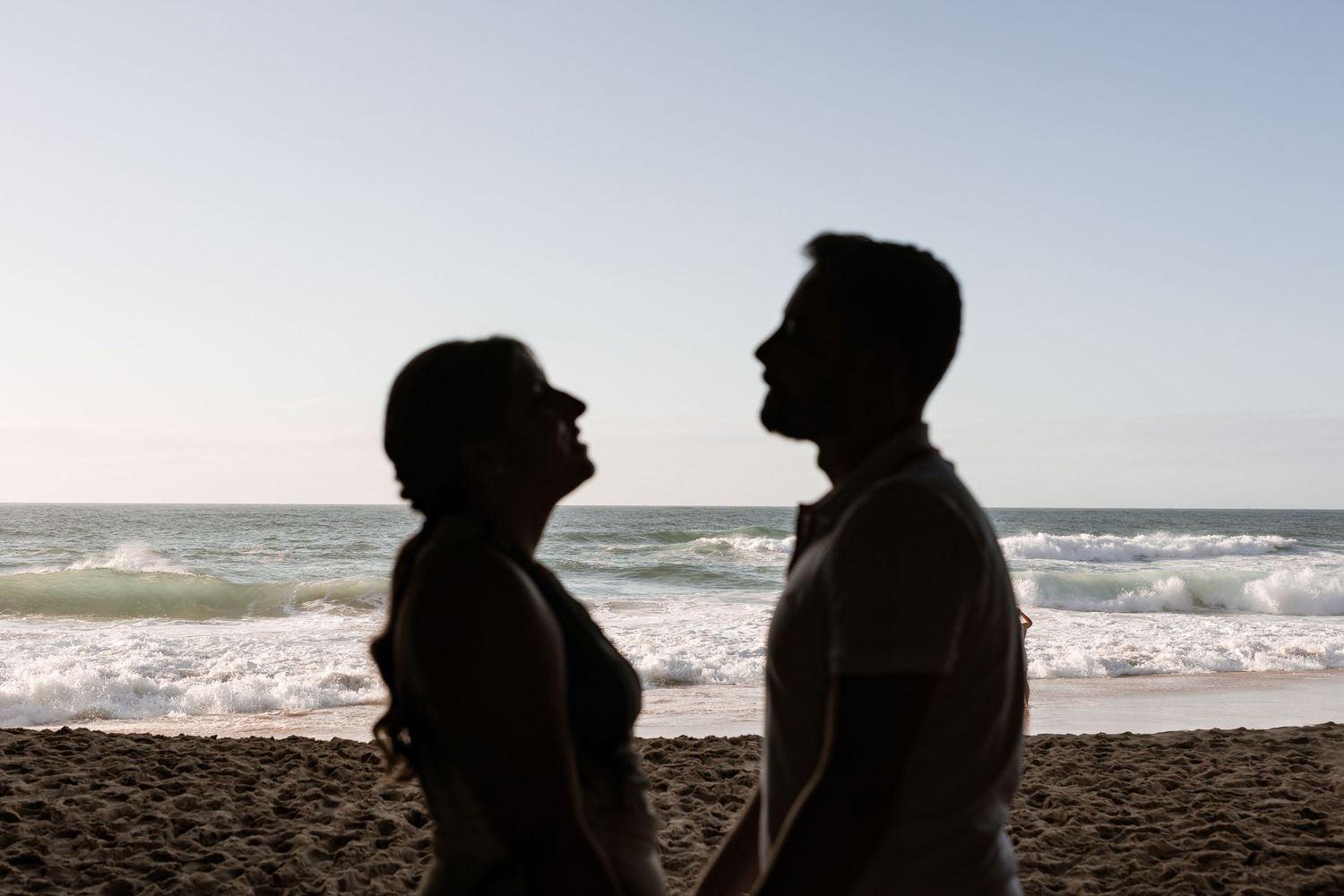 Backlit couple standing by the ocean during engagement photoshoot at Praia da Adraga Sintra