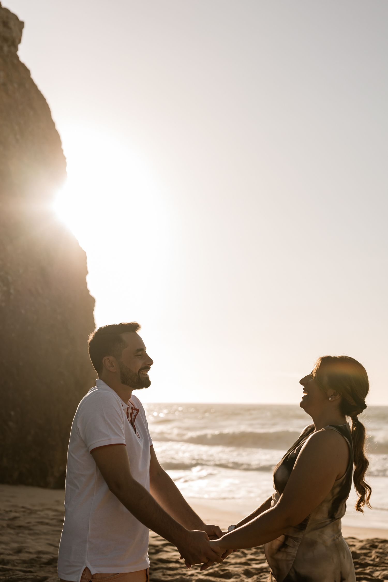 Romantic couple holding hands on the beach at sunset in Praia da Adraga Sintra