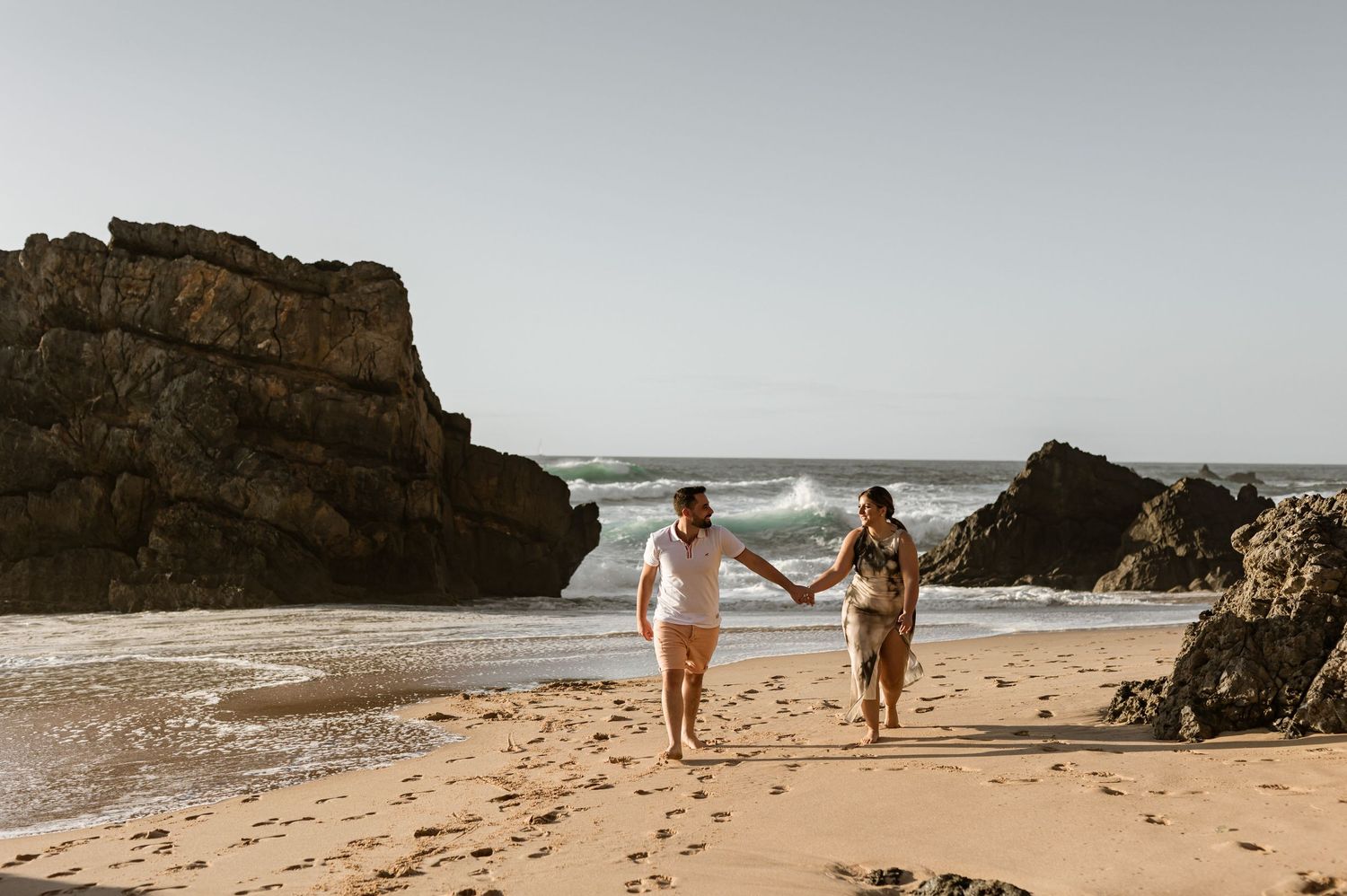 Couple walking barefoot on the beach with cliffs and waves at Praia da Adraga Portugal