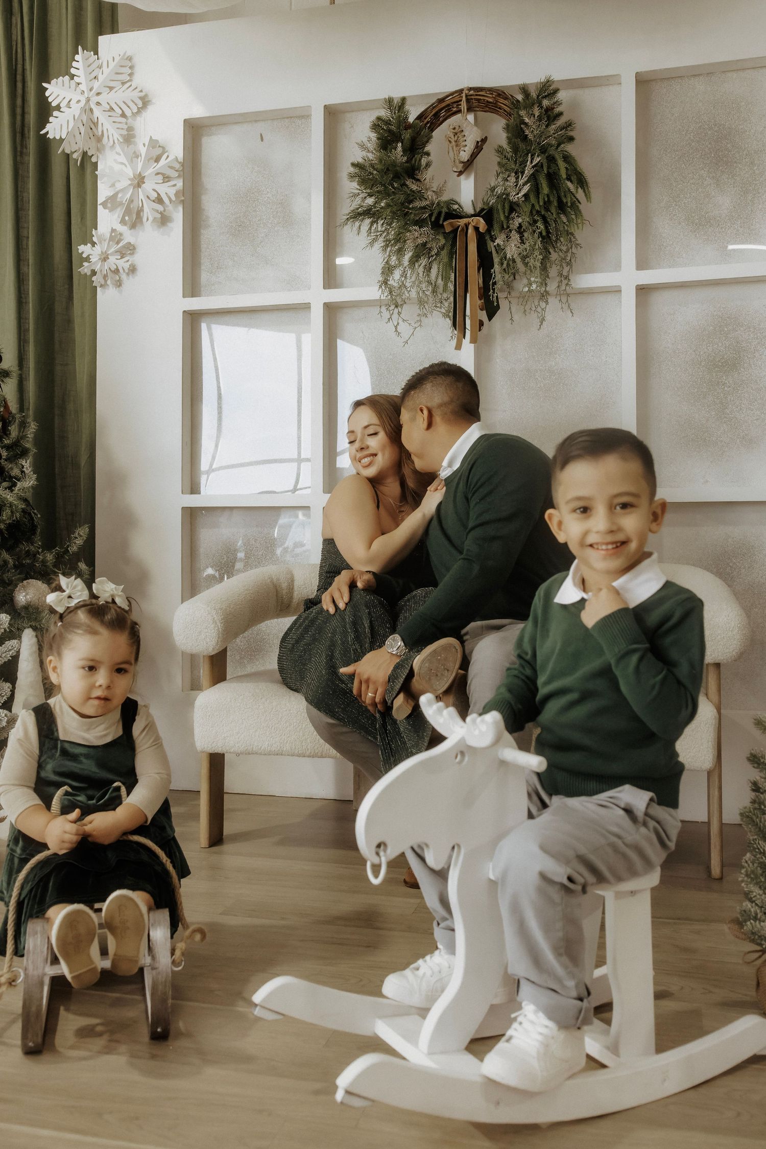 Mom and dad kiss while son and daughter play with rocking horses smiling