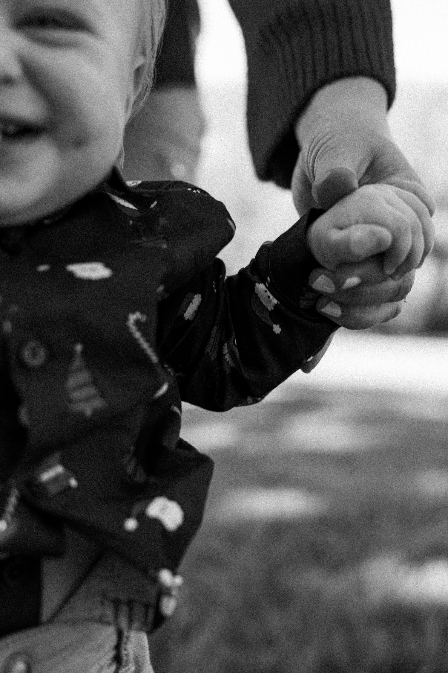 Black and white photo of a laughing baby holding an adults hand outdoors.