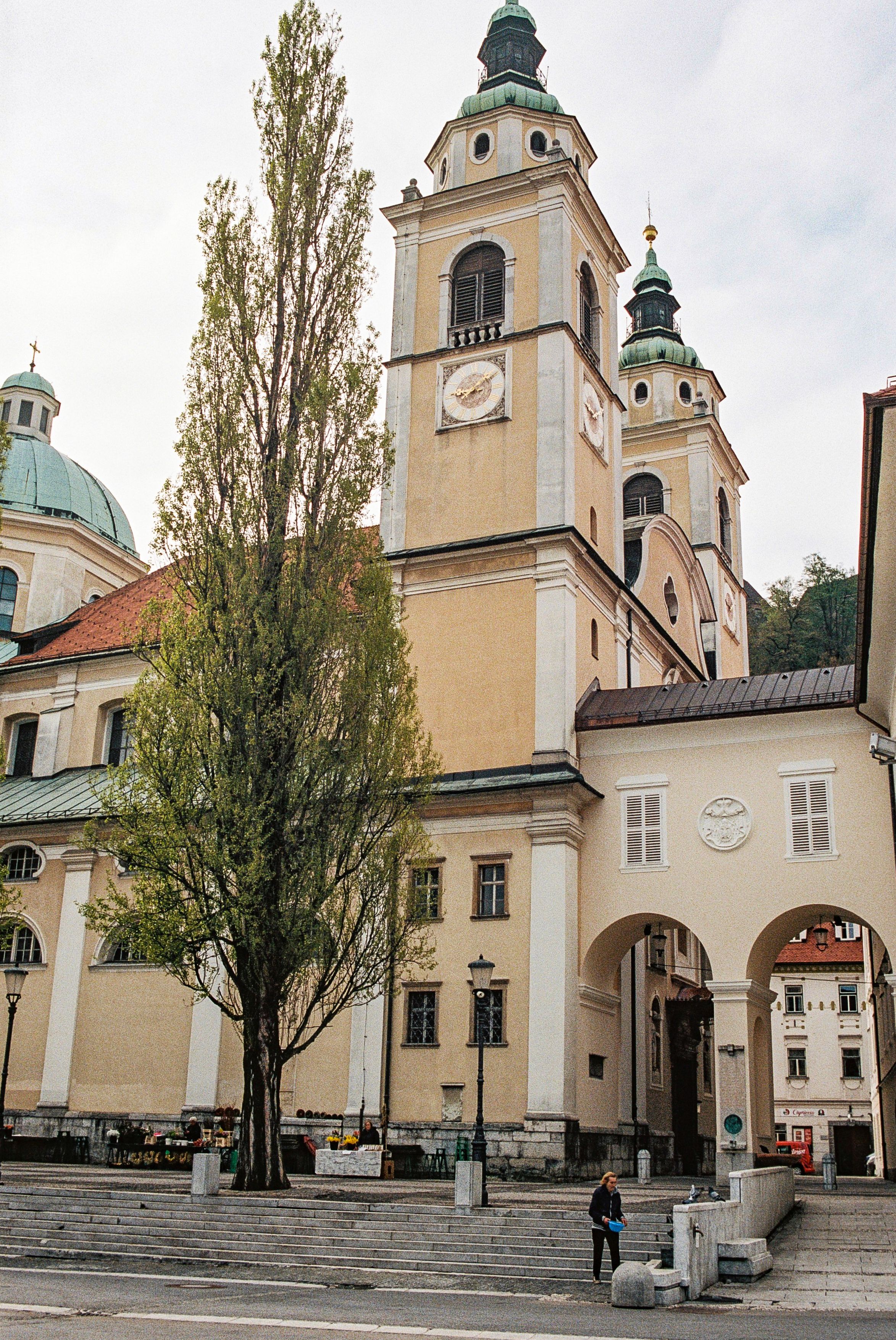 Tall beige cathedral with twin bell towers and green domes in Ljubljana's old town.