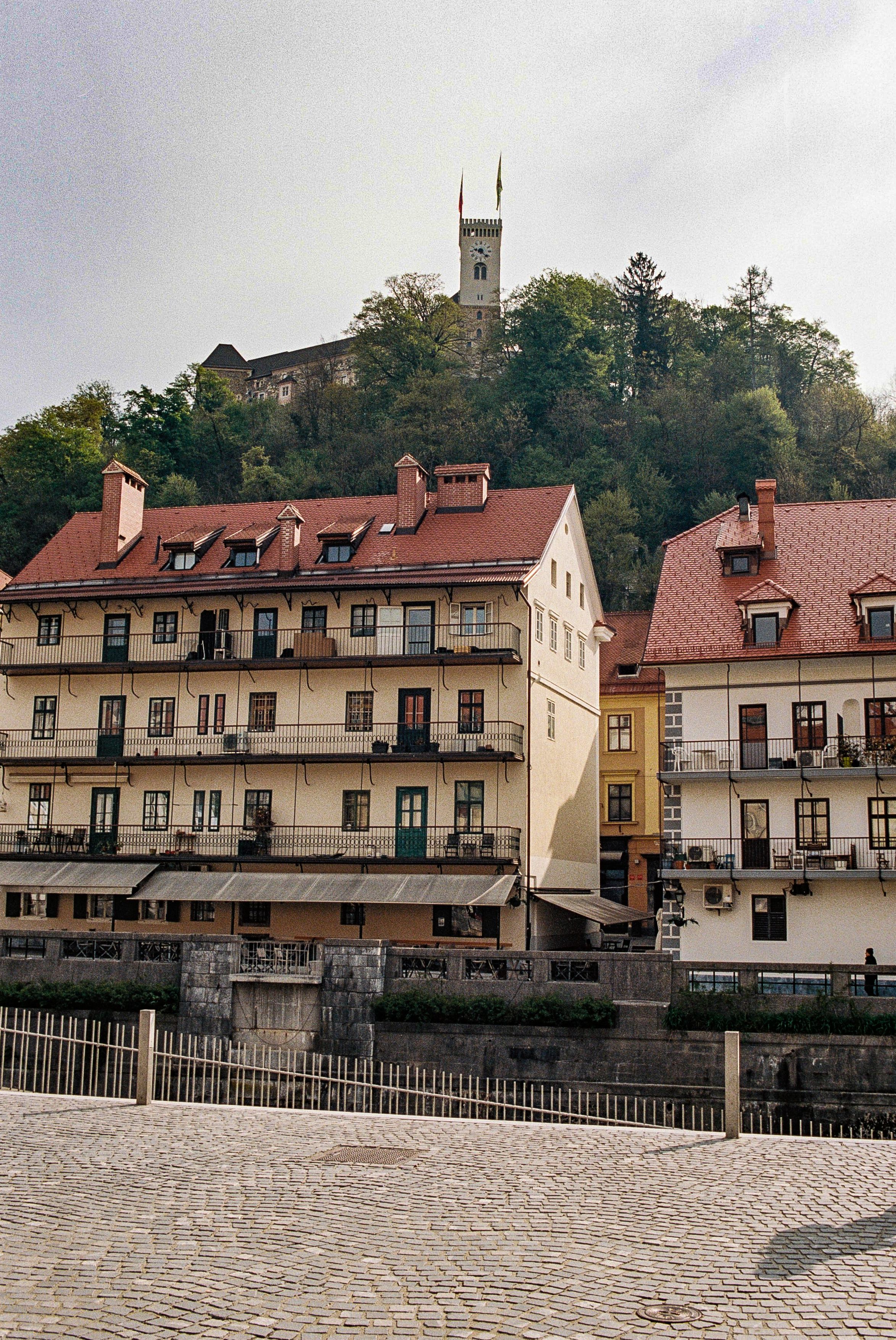 Historic buildings with red-tiled roofs nestled on a hillside beneath a towering church spire in Ljubljana, Slovenia.