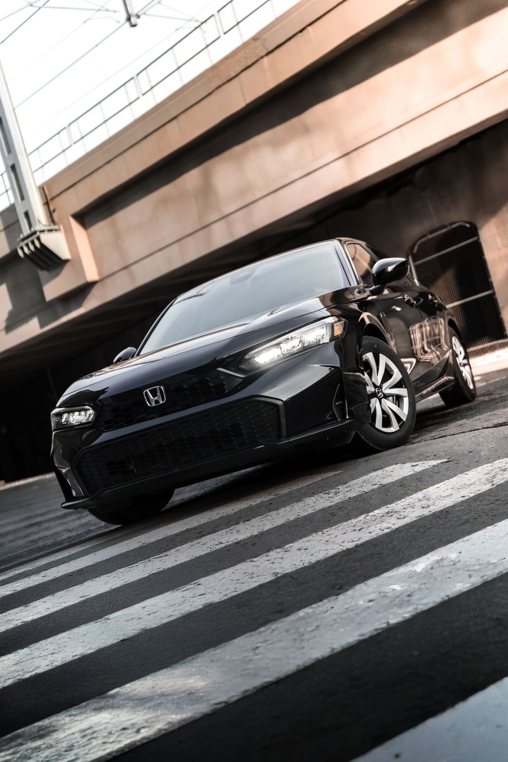 Front view of black Honda Civic on zebra crossing beneath industrial structure.Mtlshutter photography