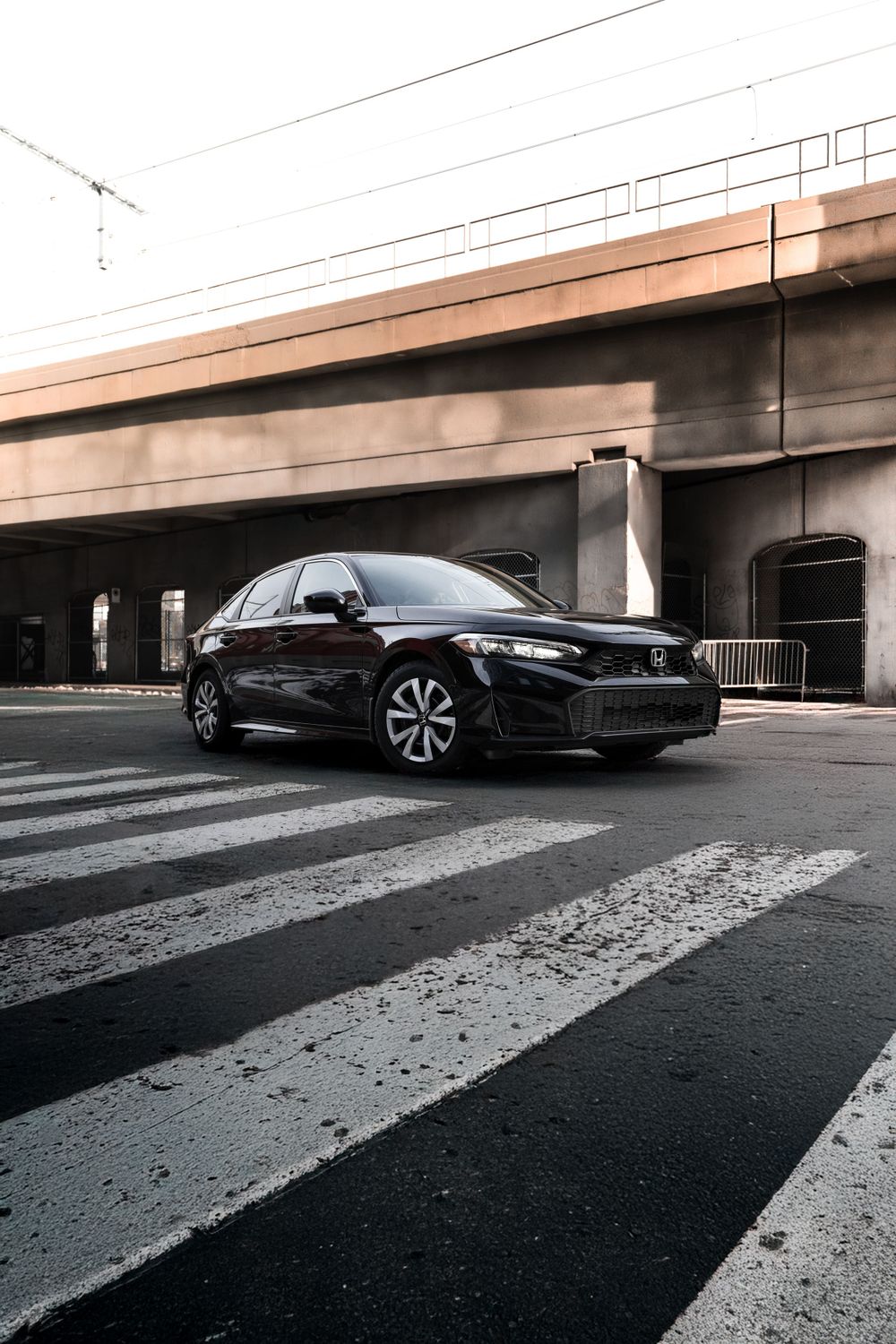 Black Honda sedan positioned on striped crosswalk under concrete overpass with moody urban backdrop. Mtlshutter photography