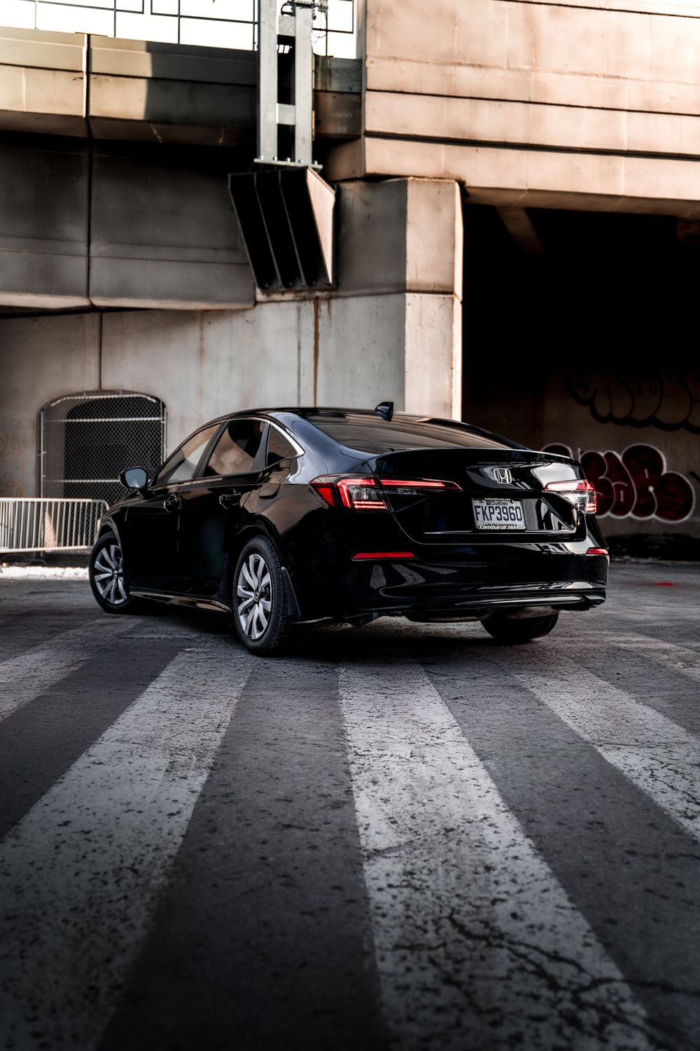 Rear three-quarter view of black Honda sedan on striped crosswalk under urban architecture. Mtlshutter photography