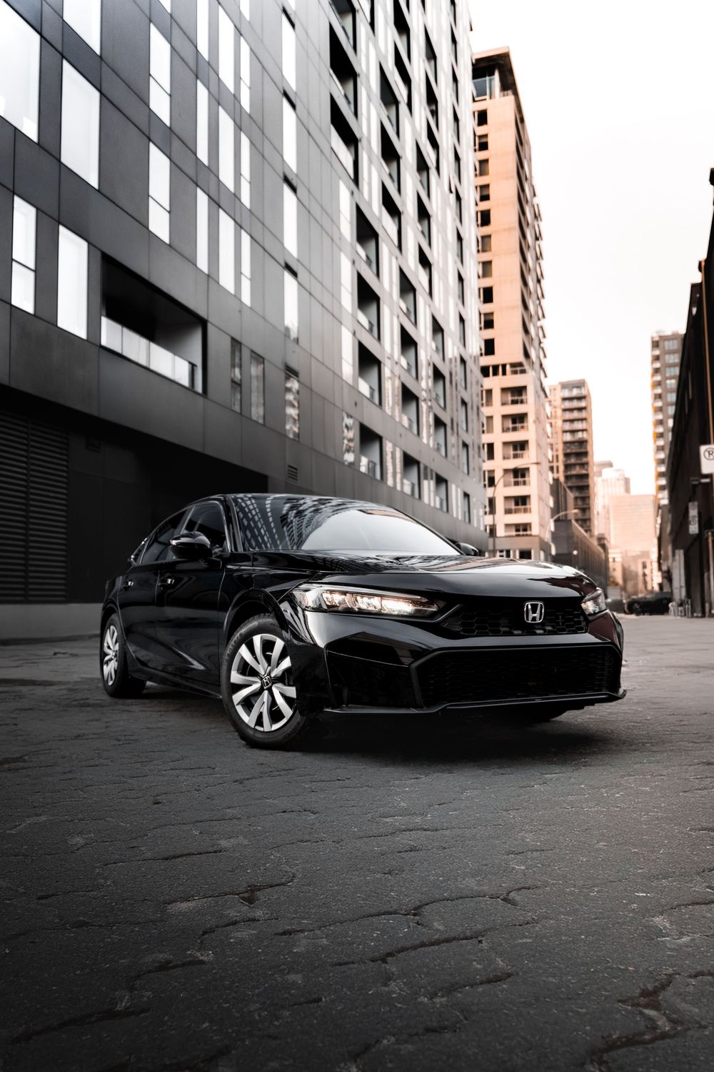 Black Honda sedan parked in urban setting with modern high-rise buildings in background. Mtlshutter photography