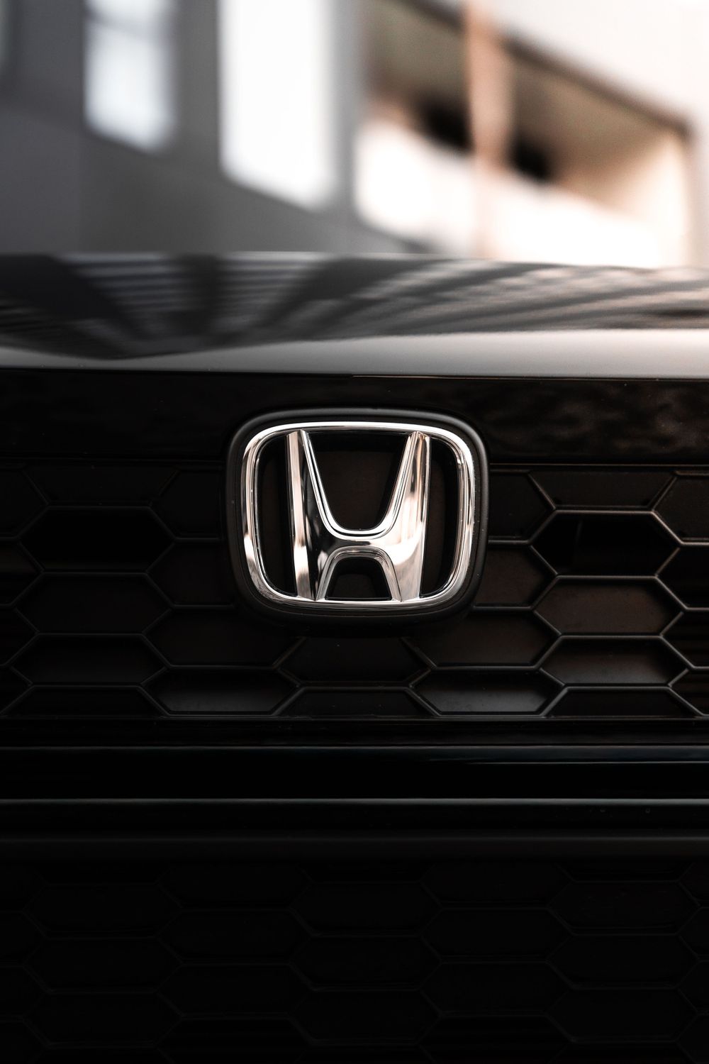 Close-up of chrome Honda emblem on black honeycomb grille pattern. Mtlshutter photography