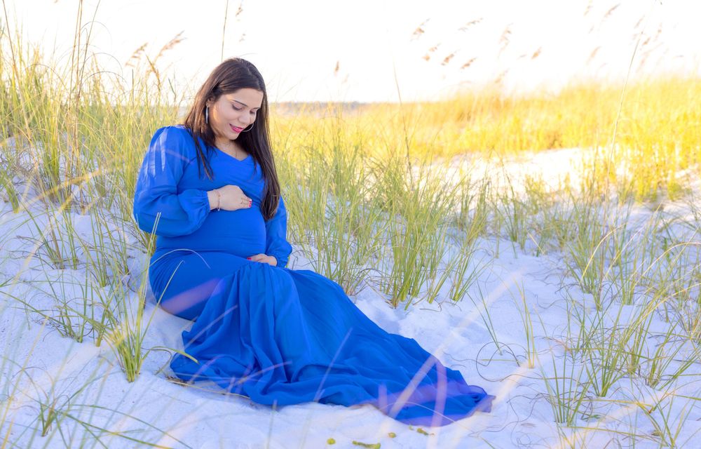 Person in flowing royal blue dress sitting peacefully on white sand dunes during golden sunset.