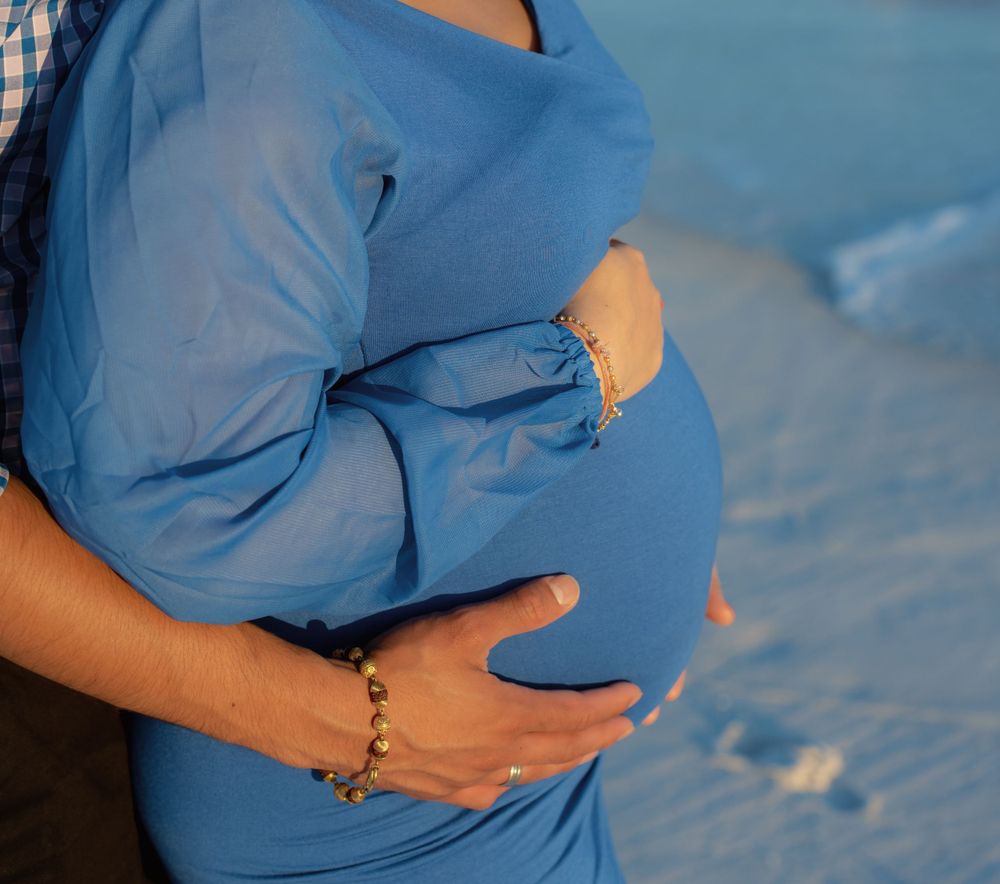 Close-up of a pregnant woman's belly in a flowing blue dress being gently cradled.